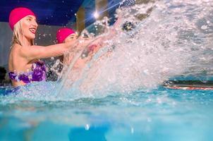 beautiful amazing slim young stylish women in colorful swimming suits and pink swimming hats in swimming pool photo