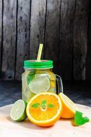 Can with cold and fresh lemonade. Lemon, orange, lime and mint on wooden background. photo