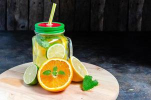 lata con limonada fría y fresca. limón, naranja, lima y menta sobre fondo de madera. foto
