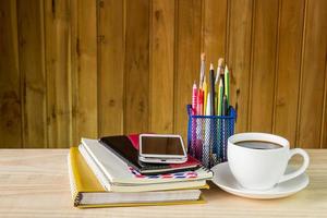 cuaderno, teléfono inteligente, taza de café y pila de libros sobre una mesa de madera foto