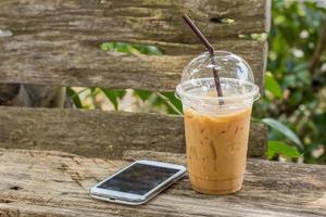 Ice coffee and smart phone on wooden table photo