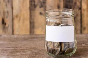Coins in a glass jar on wooden table photo