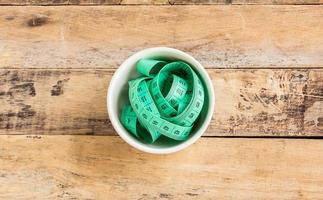 Green measuring tape in ceramic cup on wooden table