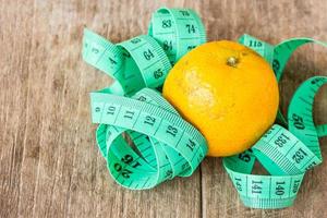 Green measuring tape and tangerine on wooden table photo