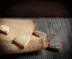 deliciosas galletas caseras en forma de corazón espolvoreadas con azúcar glaseado sobre tela de saco y tablas de madera. imagen horizontal foto