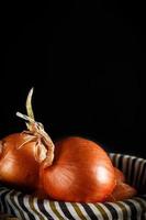 Still life of onions with wicker basket with black background. Rustic style. Vertical image. photo