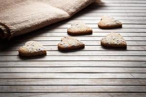 deliciosas galletas caseras en forma de corazón espolvoreadas con azúcar glas sobre una tabla de madera con tela de saco en el fondo. imagen horizontal vista a contraluz. foto