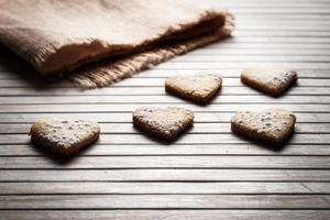 Delicious heart-shaped homemade cookies sprinkled with icing sugar on a wooden board with sackcloth in the background. Horizontal image seen against backlight. photo