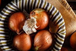 Still life of onions and garlic head in a wicker basket on a sackcloth and wooden boards. Seen from above. Rustic style. Horizontal image. photo