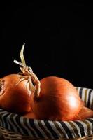 Still life of onions with wicker basket with black background. Rustic style. Vertical image.