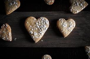 Delicious home-made heart-shaped cookies sprinkled with icing sugar in a wooden board. Horizontal image seen from above. Dark moody style. photo