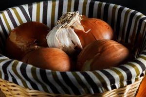 Onions and head of garlic in a wicker basket seen from up close. Rustic style. Horizontal image. photo