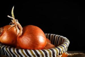 Still life of onions with wicker basket with black background. Rustic style. Horizontal image. photo