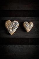 Two delicious home-made heart-shaped cookies sprinkled with icing sugar in a wooden board. Vertical image seen from above.Concept of love in couple. Dark moody style.
