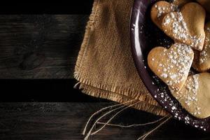 deliciosas galletas caseras en forma de corazón espolvoreadas con azúcar glaseado sobre tela de saco y tablas de madera. imagen horizontal vista desde arriba. foto