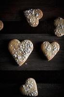 Delicious home-made heart-shaped cookies sprinkled with icing sugar in a wooden board. Vertical image seen from above. Dark moody style.