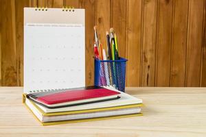 cuaderno, bolígrafo, lápiz y pila de libros con calendario sobre mesa de madera