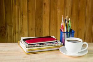cuaderno, taza de café y pila de libros sobre una mesa de madera