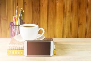 teléfono inteligente, taza de café y pila de libros sobre fondo de mesa de madera.