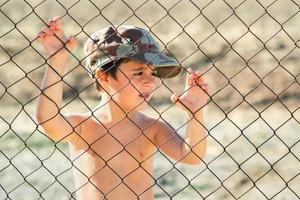 Sad child in a military cap behind a fence. Stop war concept photo