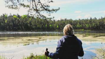 vista aérea ascendente mulher caucasiana loira idosa fica segurando varas nórdicas vermelhas e desfrutando do lago e da natureza tranquila da floresta verde video