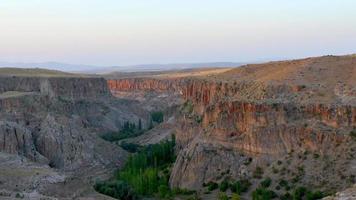 Zoom out view scenic ihlara valley rock cliffs with beautiful textures on sunset with green tree valley video