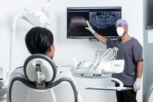 Dentist pointing at a x-ray in front of a patinet sitting on a chair in a clinic photo