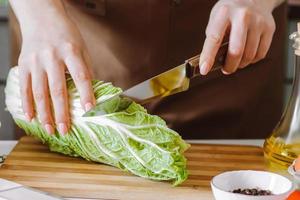 mujer joven preparando ensalada de dieta y rebanando repollo chino. foto