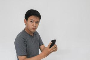 Wow face of Your Asian man shocked what he see in the smartphone on isolated grey background. photo