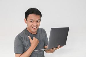 Young Asian man in grey t-shirt Feeling happy and smile with holding laptop in hand. photo