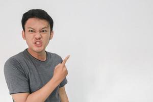 Angry and hate face of young Asian man in gray t-shirt with hand point on empty space. photo