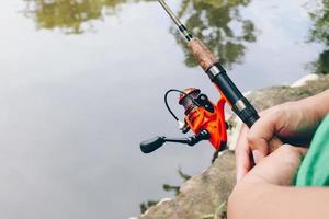 cierre de spinning con el carrete de pesca en la mano, anzuelo de pesca en la línea con el cebo en la mano izquierda contra el fondo del agua. foto