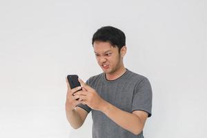 Angry Asian young man get mad on the smartphone. Indonesia Man wear black shirt Isolated grey background. photo