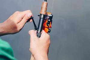 Close up of spinning with the fishing reel in the hand, fishing hook on the line with the bait in the left hand against the background of the water. photo