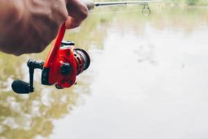 Close up of spinning with the fishing reel in the hand, fishing hook on the line with the bait in the left hand against the background of the water. photo