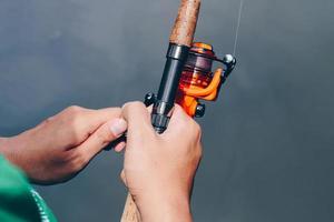 Close up of spinning with the fishing reel in the hand, fishing hook on the line with the bait in the left hand against the background of the water. photo