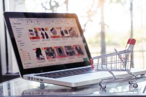 concepto de compras en línea: carrito de compras o carro y computadora portátil en la mesa foto
