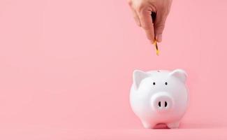 Money saving and investment concept. Hand putting coin to piggy bank on pink background with copy space photo