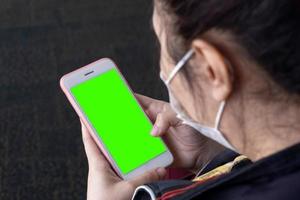 mujer asiática usa una pantalla verde de teléfono inteligente con cara de máscara quirúrgica foto