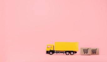 logística y servicio de entrega: camión de carga y cajas de papel o paquetes con el logotipo de un carrito de la compra sobre fondo rosa. servicio de compra en la web online y ofrece servicio a domicilio. con espacio de copia foto