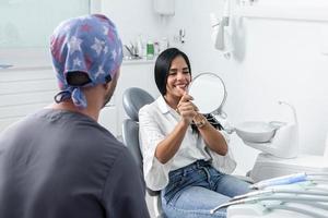 ciente sonriendo y mirándose a un espejo en una clínica dental foto