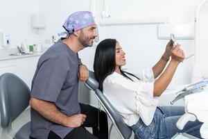 cliente mirando sus dientes en el espejo junto a un dentista en una clínica foto