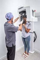 foto vertical de un dentista ajustando una máquina de blanqueamiento dental utilizada por un paciente