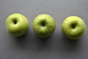 tres deliciosas manzanas verdes sobre un fondo gris foto