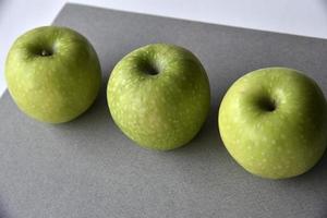 tres deliciosas manzanas verdes sobre un fondo gris foto