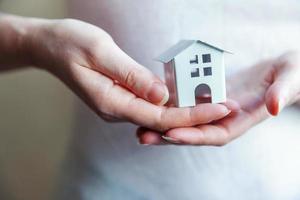 Female woman hands holding small miniature white toy house. Mortgage property insurance dream moving home and real estate concept. photo