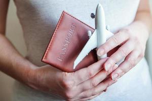 Tourist essentials. Female woman hands holding small toy model plane and passport. Travel by plane vacation summer weekend sea adventure trip journey ticket tour concept. photo