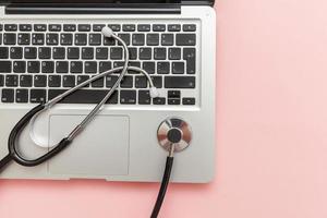 Stethoscope keyboard laptop computer isolated on pink background. Modern medical Information technology and sofware advances concept. Computer and gadget diagnostics and repair photo