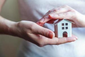 mujer mujer manos sosteniendo una pequeña casa de juguete blanca en miniatura. sueño de seguro de propiedad hipotecaria mudanza de casa y concepto de bienes raíces. foto