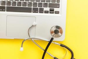 Stethoscope keyboard laptop computer isolated on yellow background. Modern medical Information technology and sofware advances concept. Computer and gadget diagnostics and repair photo